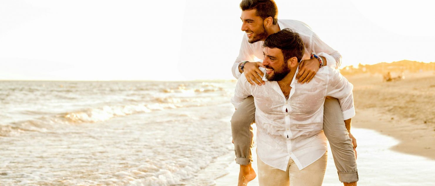 A gay man piggybacking his lover on a beach.